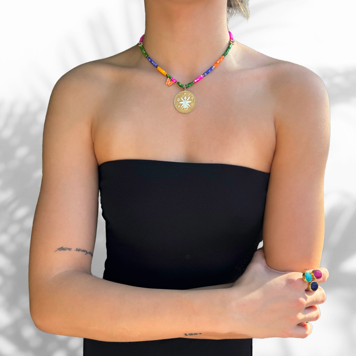 Gold pendant necklace with meditative woman, spiral, and evil eye symbols on multicolor pearls
