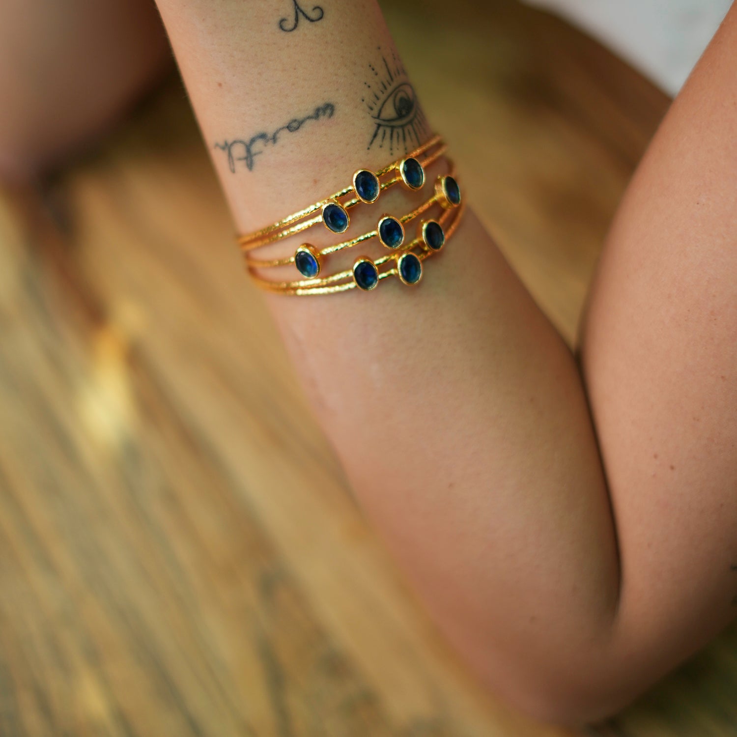 Stylish 24k gold-plated cuff bracelet with five intertwined gold wires and sapphire stones, adjustable to fit various wrist sizes.