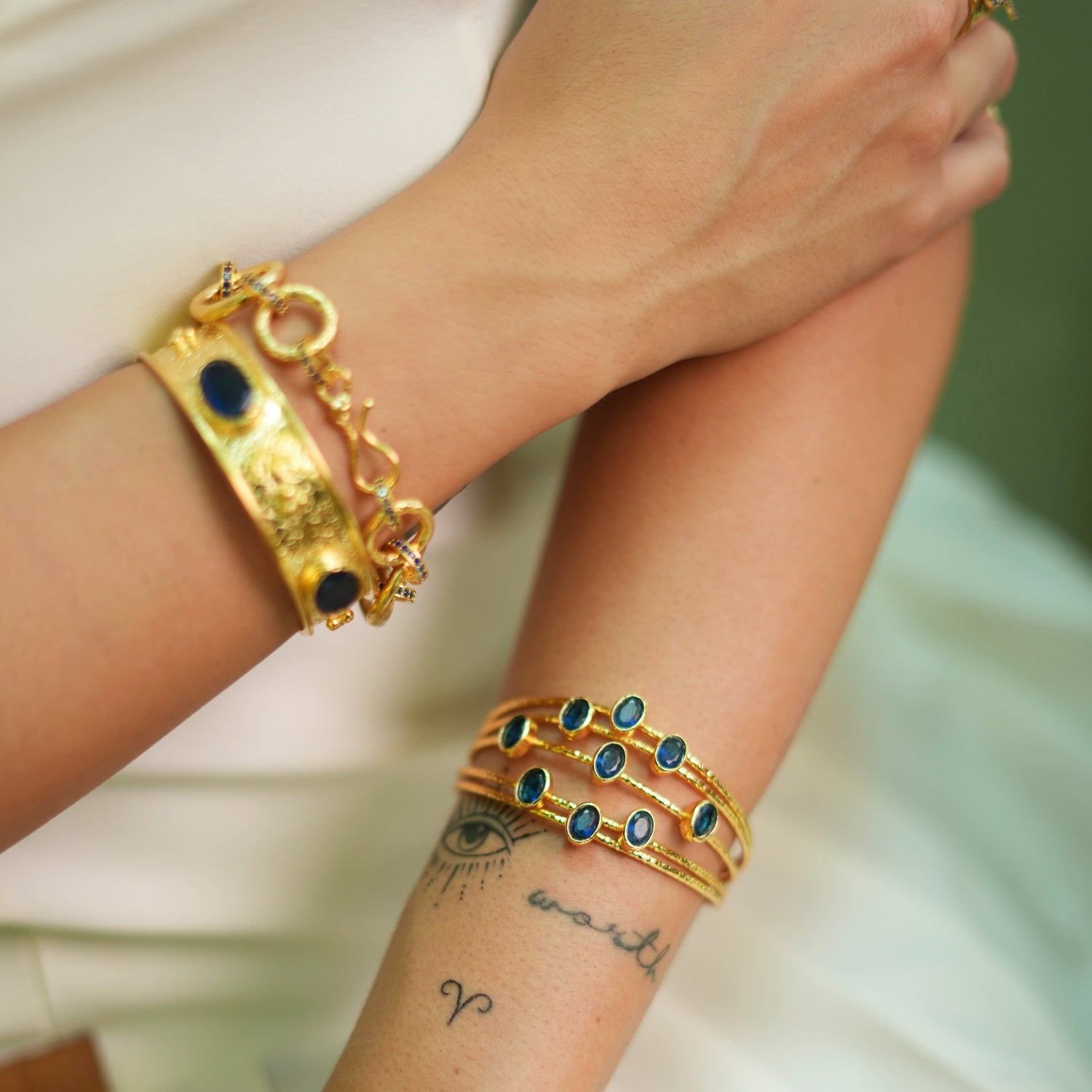 Elegant gold cuff bracelet with 24k plating, featuring five intertwined gold wires and oval sapphire stones, adjustable size.