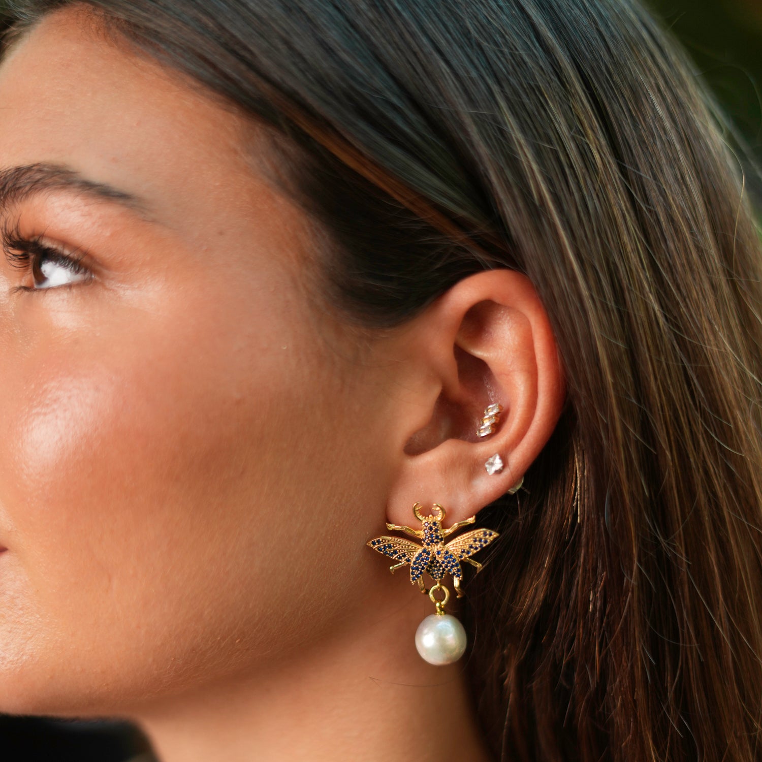 Elegant gold earrings with a queen bee design, adorned with sapphire stones and a dangling pearl, crafted in 24k gold plating.