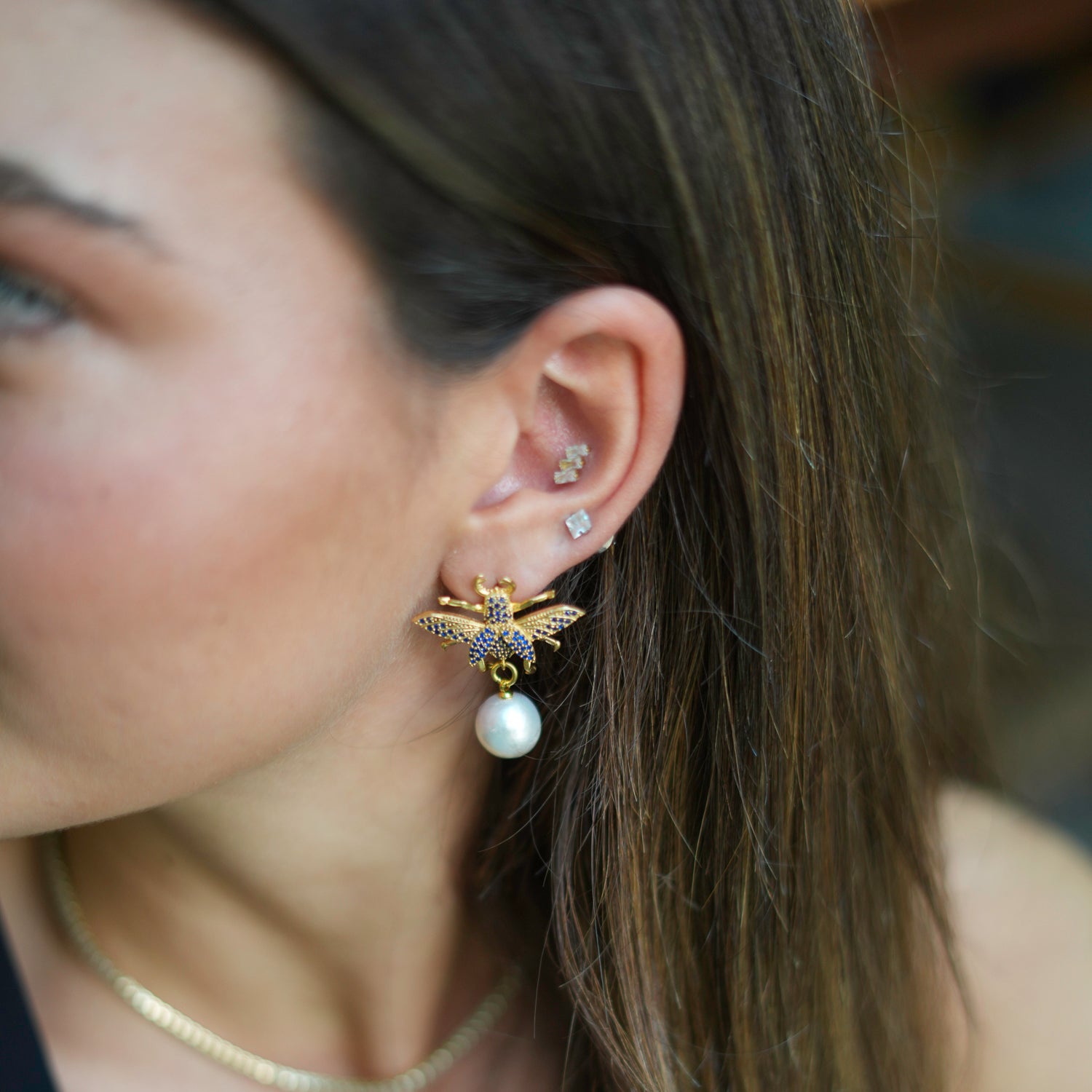 Luxurious 24k gold-plated earrings with a queen bee charm, adorned with sapphires and a pearl drop for a regal and elegant look.