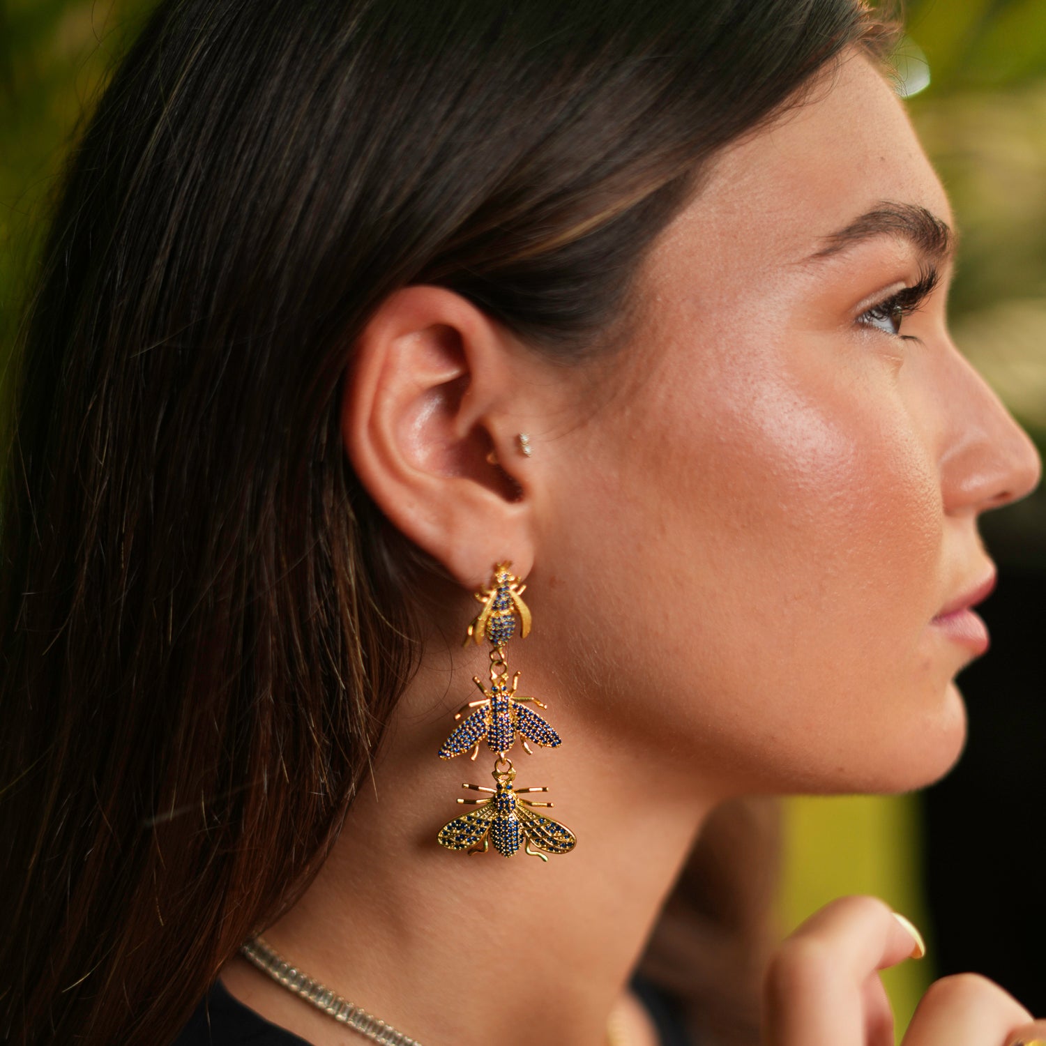 Bold gold dangle earrings with trio queen bee designs, embellished with vibrant sapphire stones for a powerful and sophisticated look.