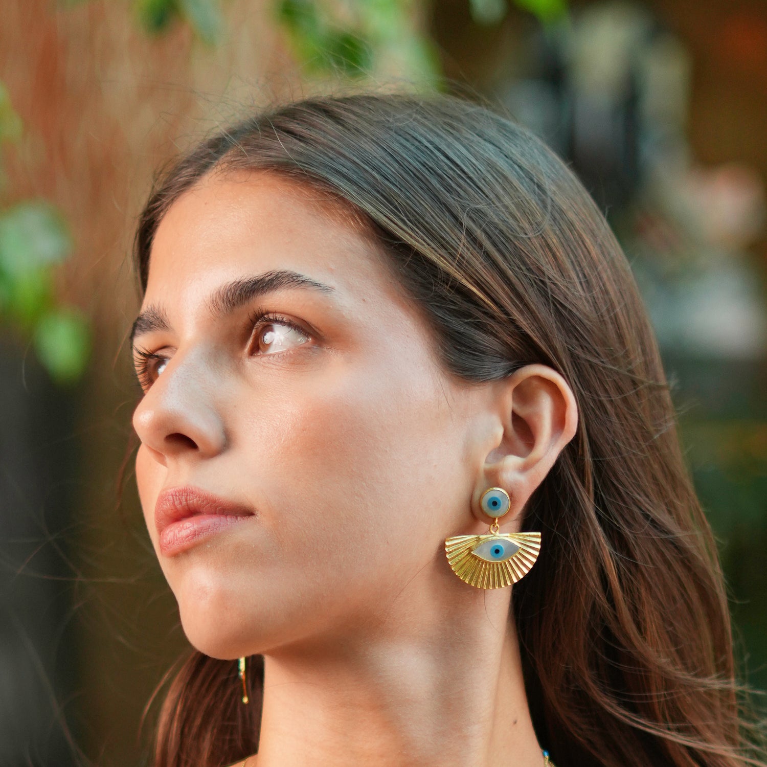 Bold 24k gold-plated earrings with evil eye studs and sun-shaped plates, accented with pearls and blue enamel for a spiritual touch.