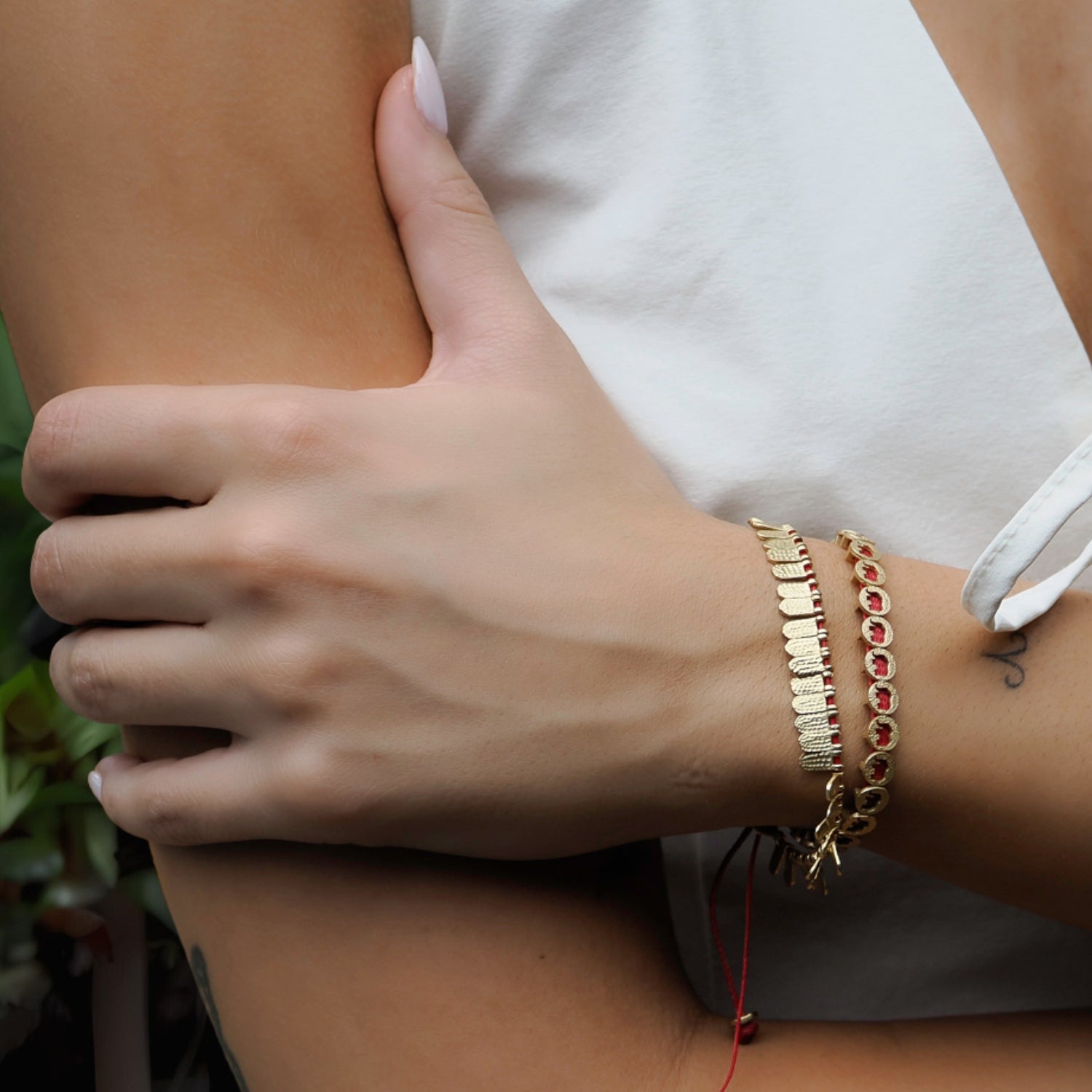 Elegant red cord bracelet with 18K gold-plated fish scale-inspired charms, perfect for layering or wearing alone.
