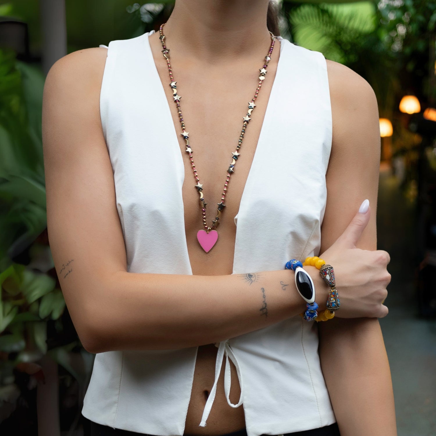 Close-up of a celestial-themed necklace with gold hematite beads and a vibrant pink enamel heart pendant.