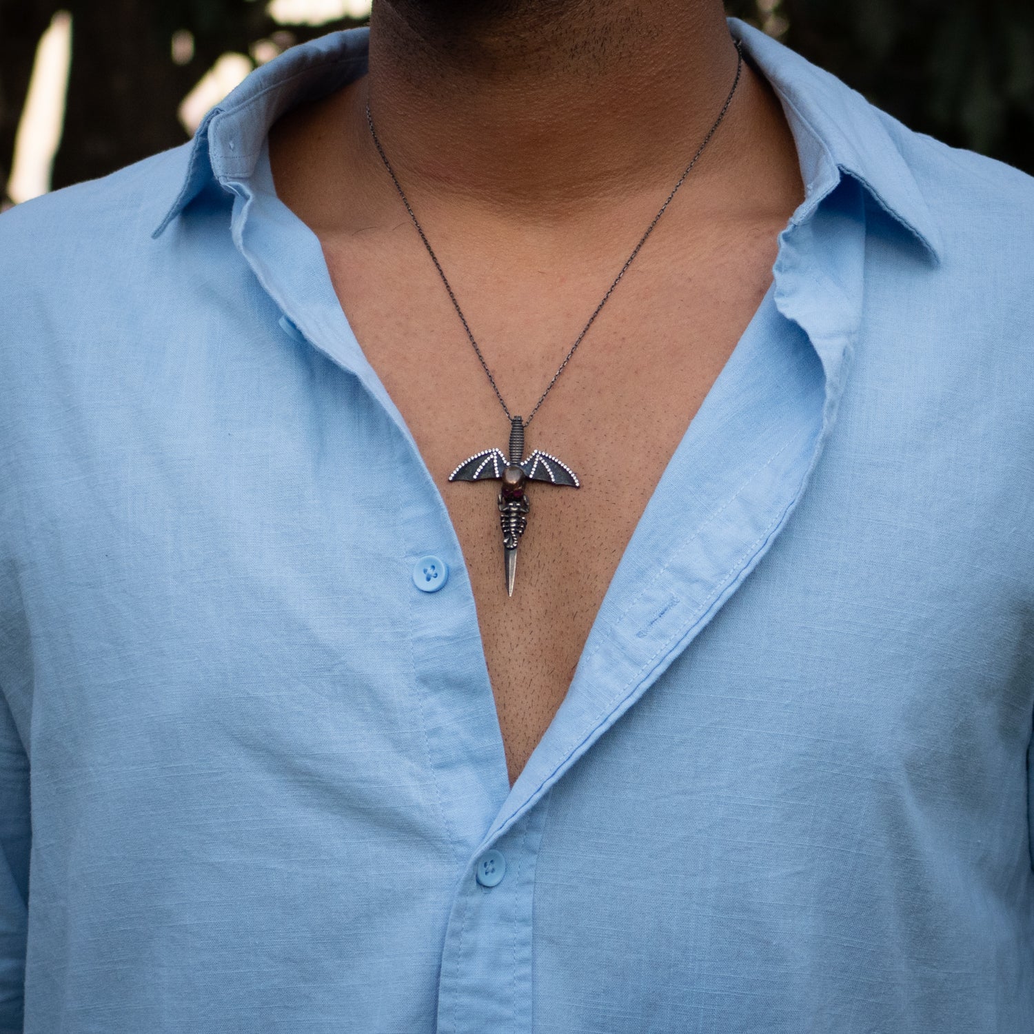 Sterling silver necklace with rhodium plated skull sword pendant featuring ruby eyes and bat wings.