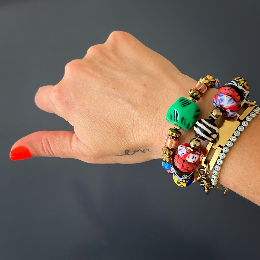 A model wearing African Colors Women Bracelet; bold geometric handmade glass and African beads with gold and green accents
