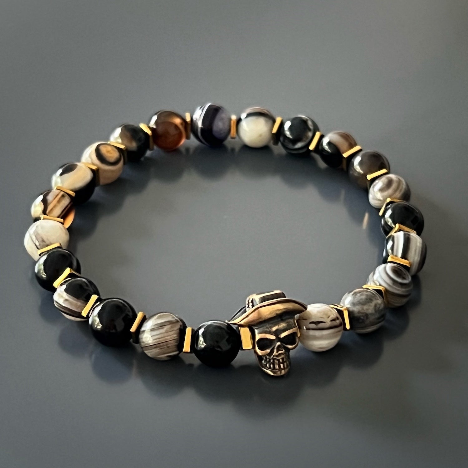The Cowboy Hat Skull Agate Bracelet features bold and unique Agate stone beads, gold hematite stone spacers, and a bronze skull charm in the shape of a cowboy hat. Handcrafted with care, this bracelet is a one-of-a-kind piece that makes a statement.