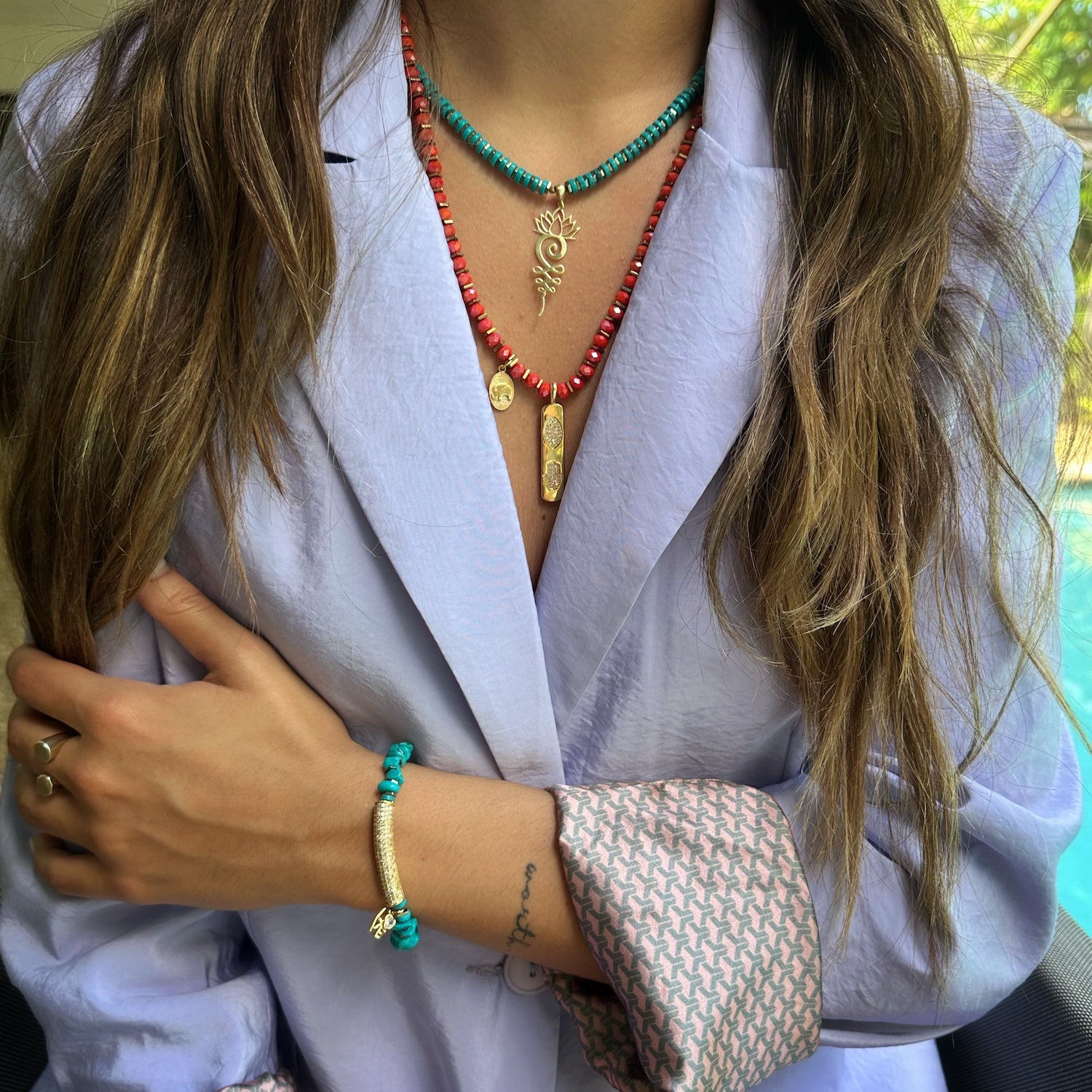 The Diamond and Turquoise Love Bracelet on a hand model, highlighting its beautiful combination of natural turquoise stone beads, gold hematite spacers, and a charm with an elephant, evil eye, and hamsa symbols. The bracelet adds a meaningful and stylish touch to the wrist.