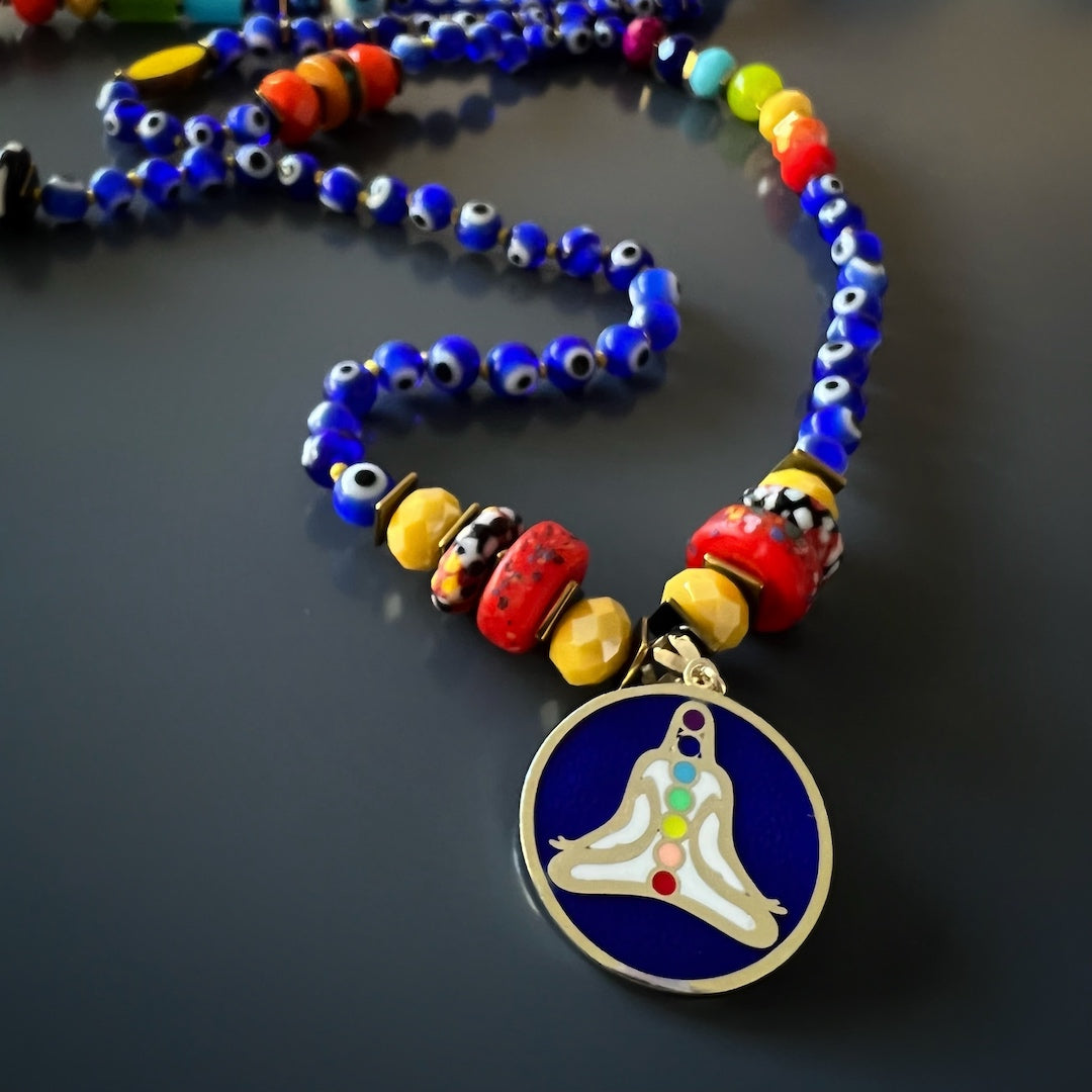 A detailed look at the 925 silver 14k gold plated chakra yoga pendant of the Evil Eye Chakra Mala Necklace. The pendant features colorful enamel and represents the seven different chakras, enhancing balance and spiritual well-being.