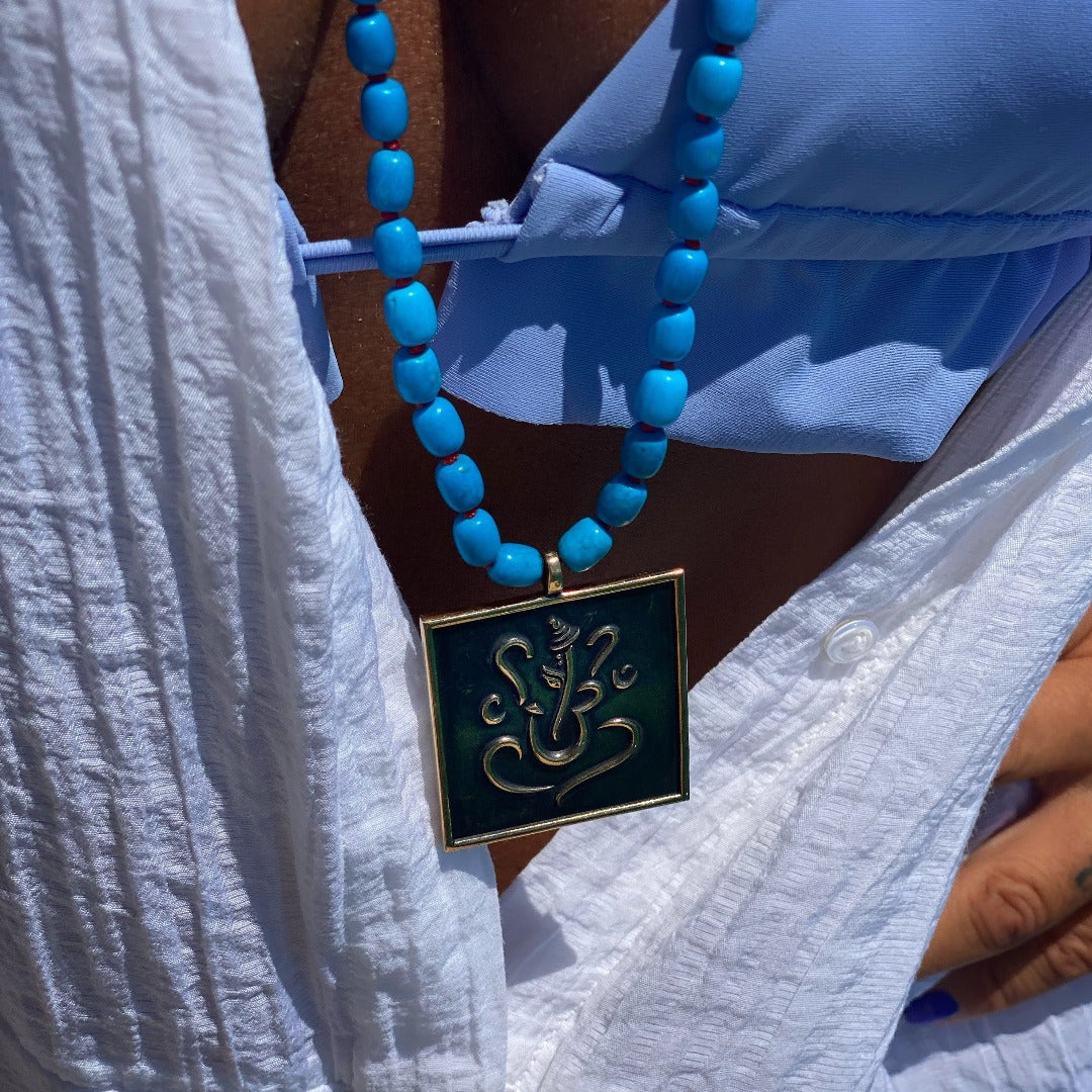 The necklace enhances the model's look with its vibrant turquoise beads and meaningful pendant.