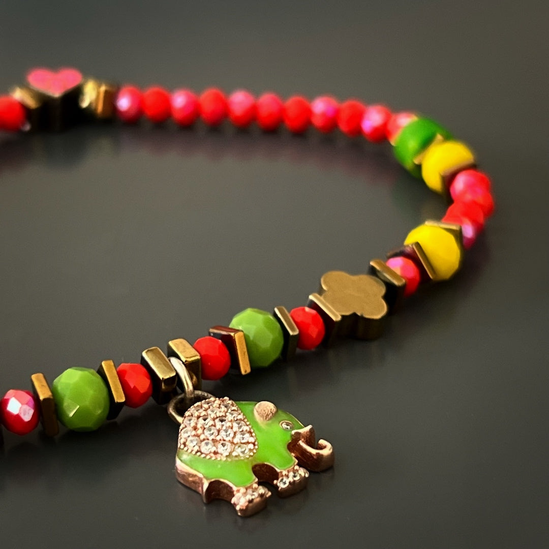 Discover the protective powers and positive symbolism of the Powerful Symbol Anklet, adorned with red crystal beads, green jasper beads, a gold color hematite floral bead, and intricate silver charms representing the evil eye, elephant, and lucky horse shoe.