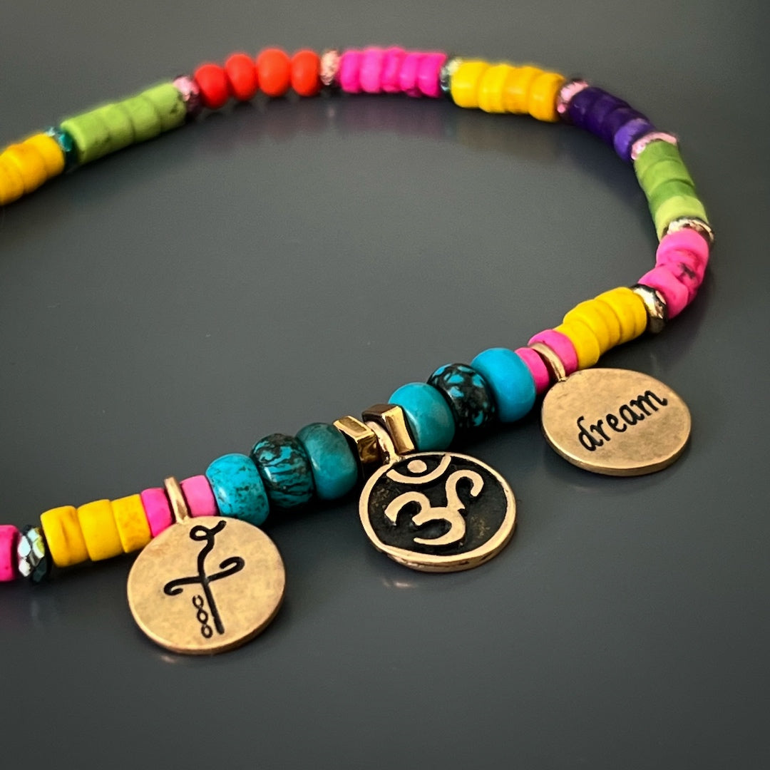 Close-up of Om-Dream-Heal charm anklet with blue and gold beads.