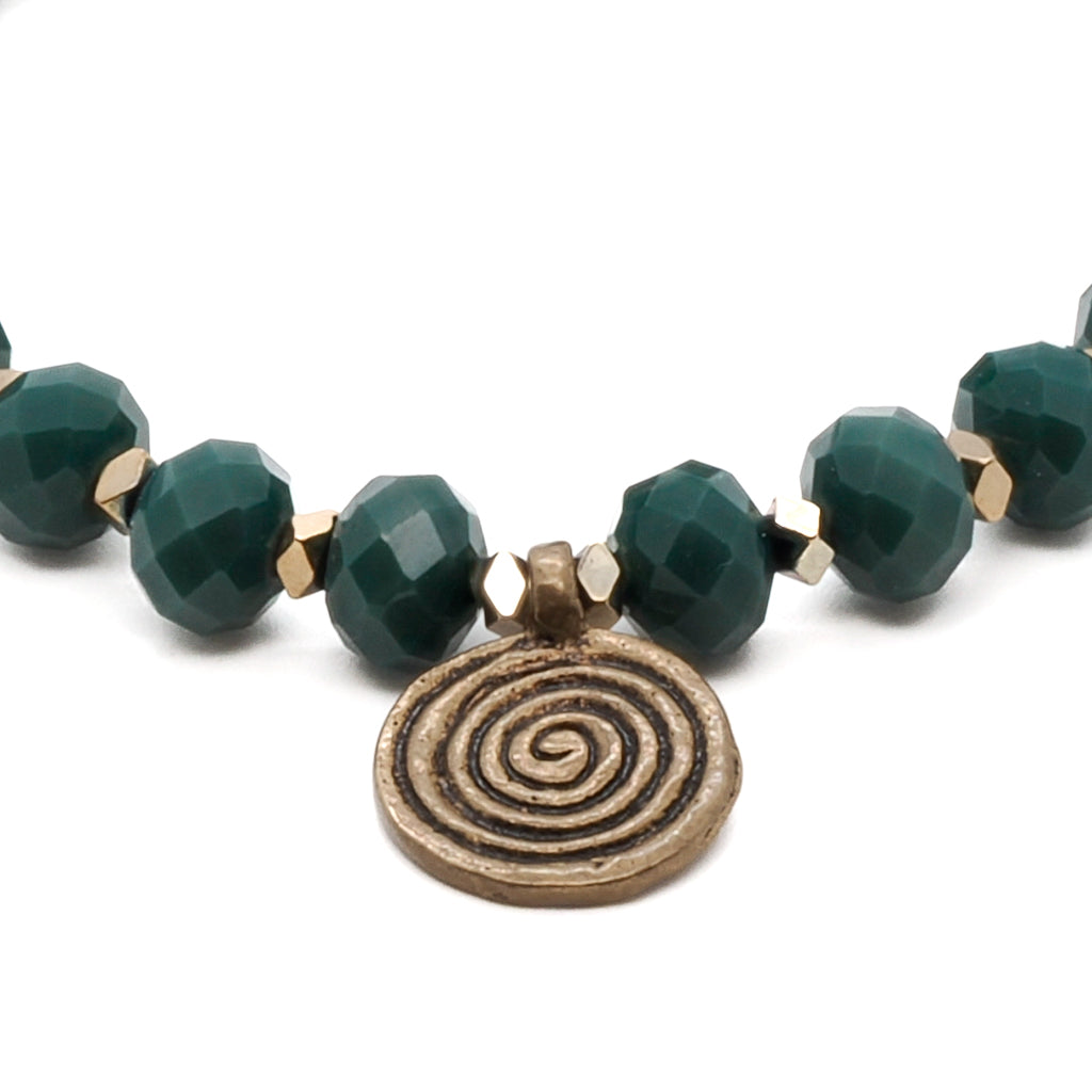 A stylish and enchanting Green Spiral Bracelet featuring a combination of green crystal beads, gold hematite spacers, a big green eye Nepal bead, and a brass spiral charm.