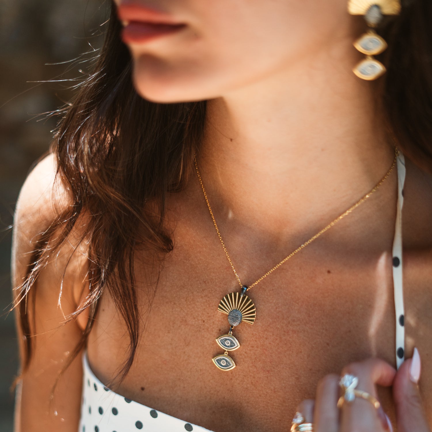 Close-up of the Sunray Ancient Eye Two-Tone Pendant Necklace worn against sunlit skin with the matching earrings visible