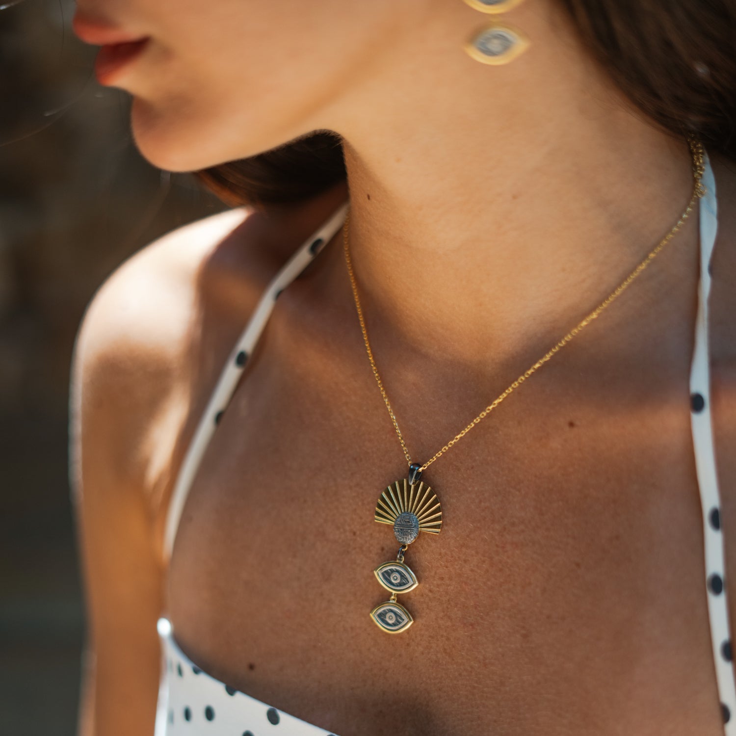 Close-up of the Sunray Ancient Eye Two-Tone Pendant Necklace worn in golden hour light with the matching earring visible
