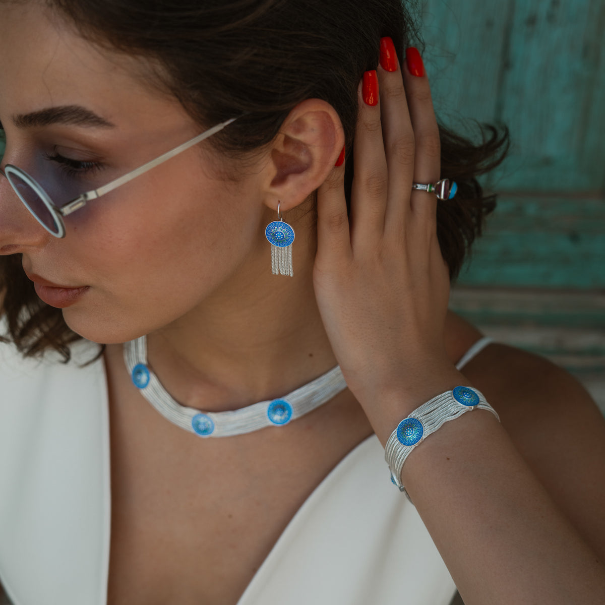 Profile view of the cobalt enamel tassel earring worn with the choker and woven bracelet