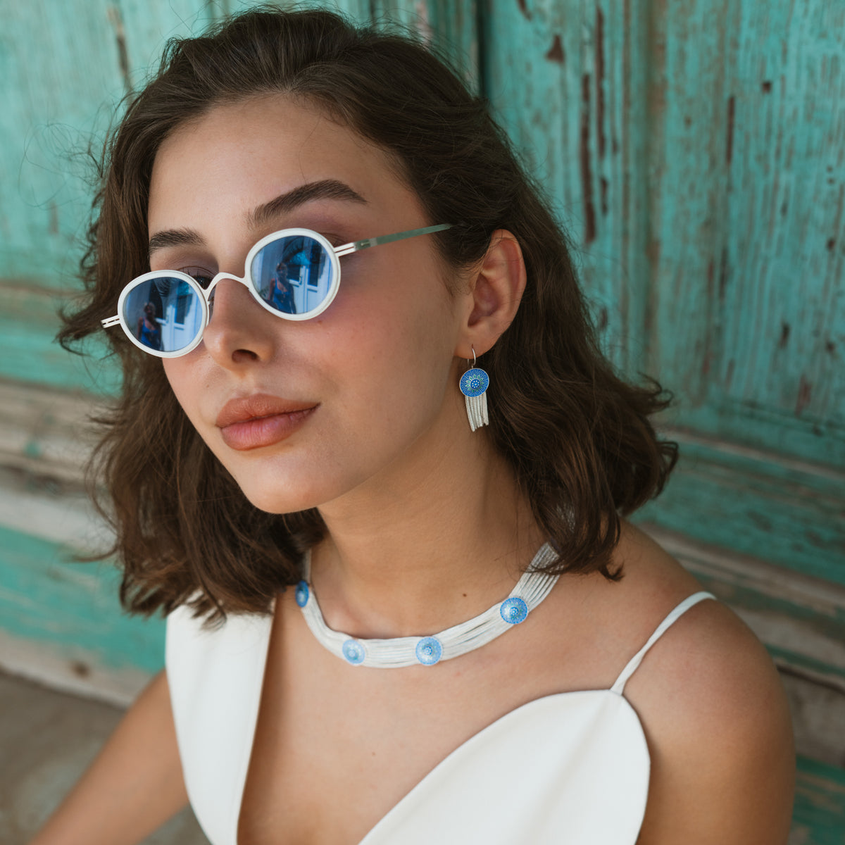 Model against a weathered blue door wearing the cobalt enamel tassel earrings and matching choker
