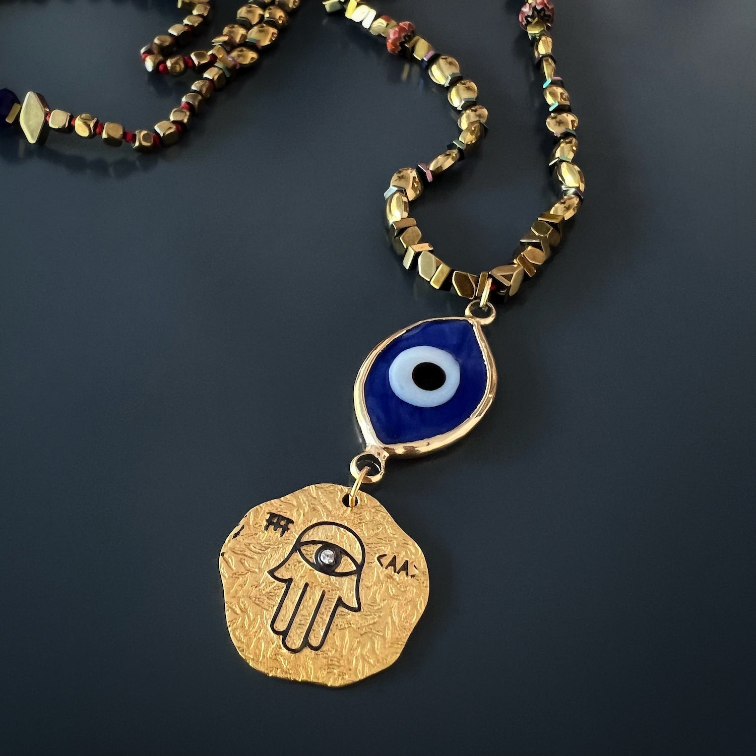 Hamsa and Evil Eye Pendant Close-Up - A close-up view of the sterling silver Hamsa pendant and the 18k gold-plated evil eye glass pendant, revealing the intricate details and craftsmanship of these powerful symbols.