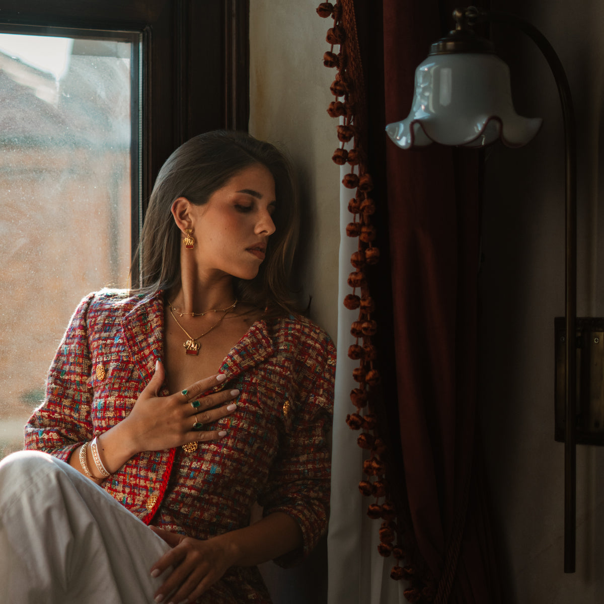 Model seated by a window wearing the Lucky Elephant Red Coral Gold Pendant Necklace with layered gold chains