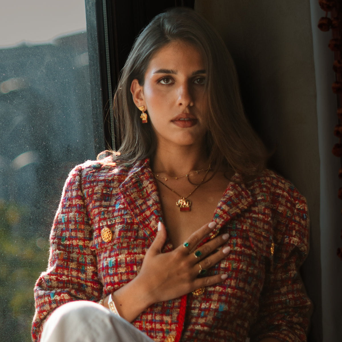 Model in a red tweed jacket wearing the Lucky Elephant Red Coral Gold Pendant Necklace with the matching elephant drop earrings