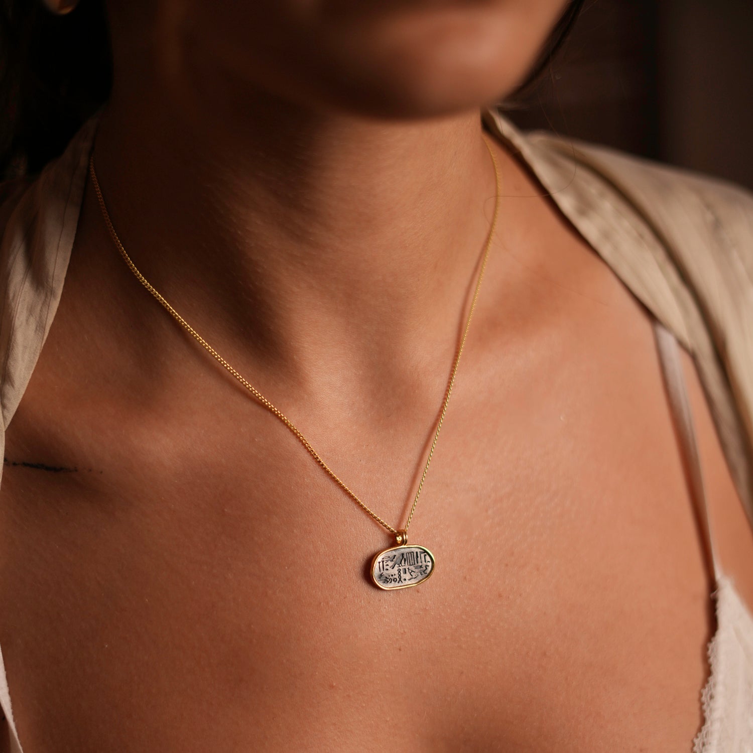 Minimalist necklace featuring a sterling silver oval pendant with Egyptian symbols, encased in a gold-plated frame.