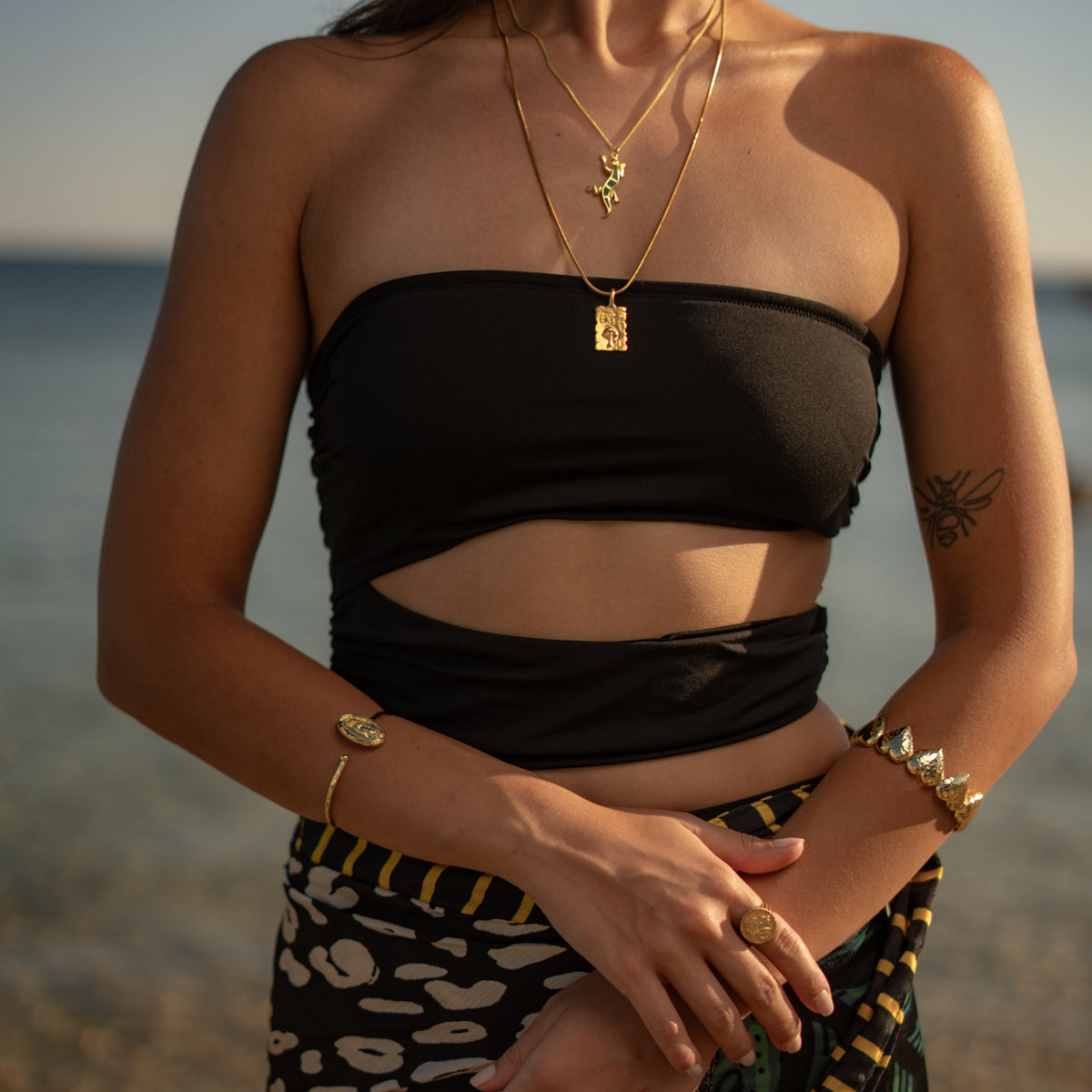 Model by the sea wearing the Virgin Mary Medallion Gold Bangle Bracelet with layered gold necklaces