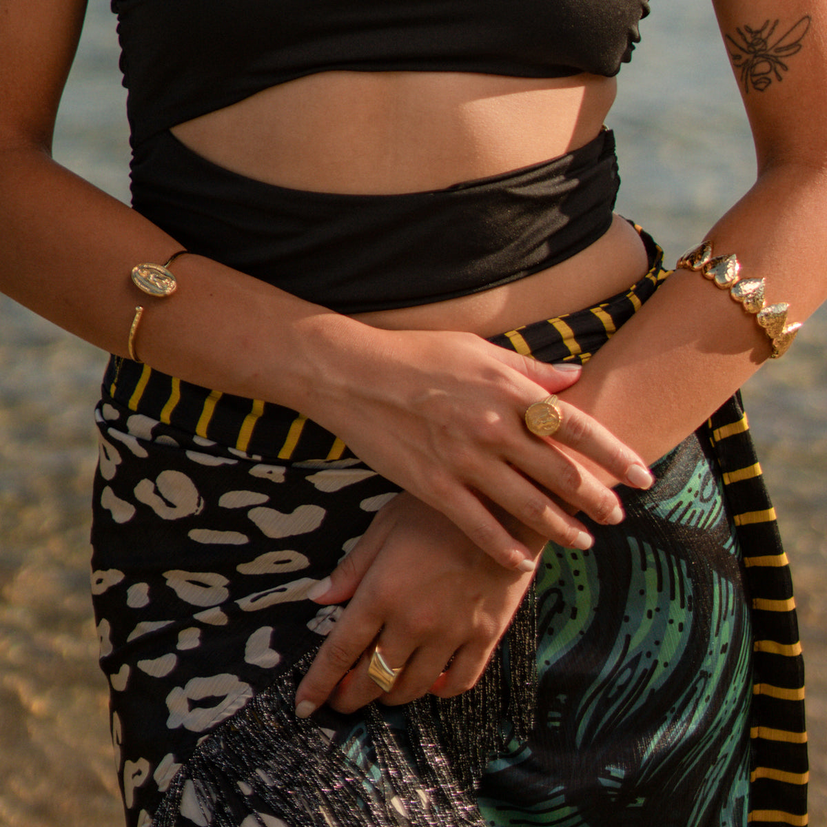 Model on the beach with crossed arms wearing the Virgin Mary medallion gold bangle