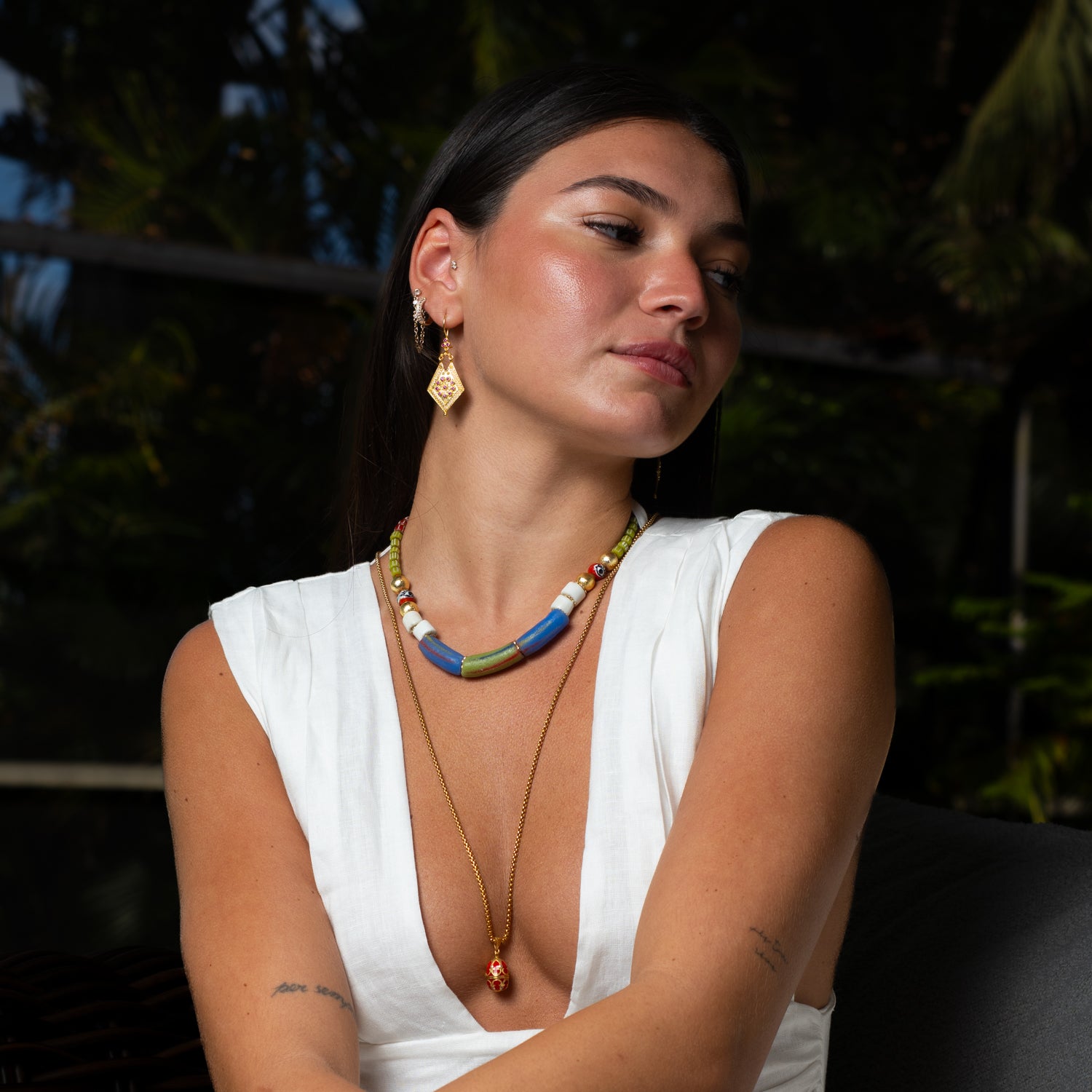Model wearing handmade African bead and evil eye statement choker by Ebru Jewelry, layered with a long gold pendant necklace and a white linen dress.