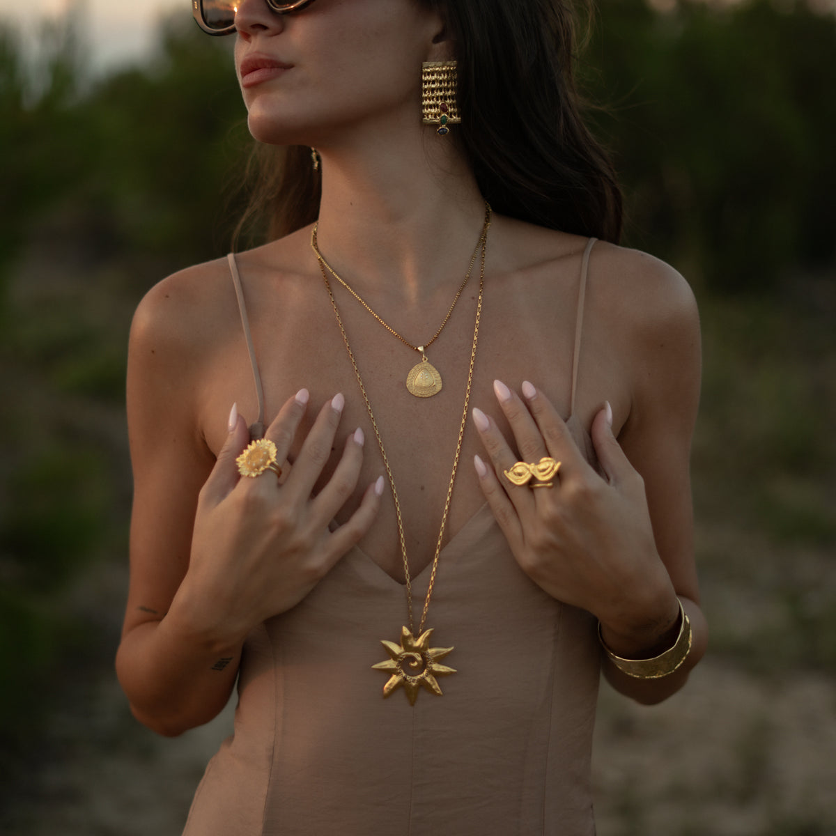 Woman at dusk wearing the All Seeing Eyes gold ring with a sunflower ring, a gold sun pendant and a hammered gold cuff