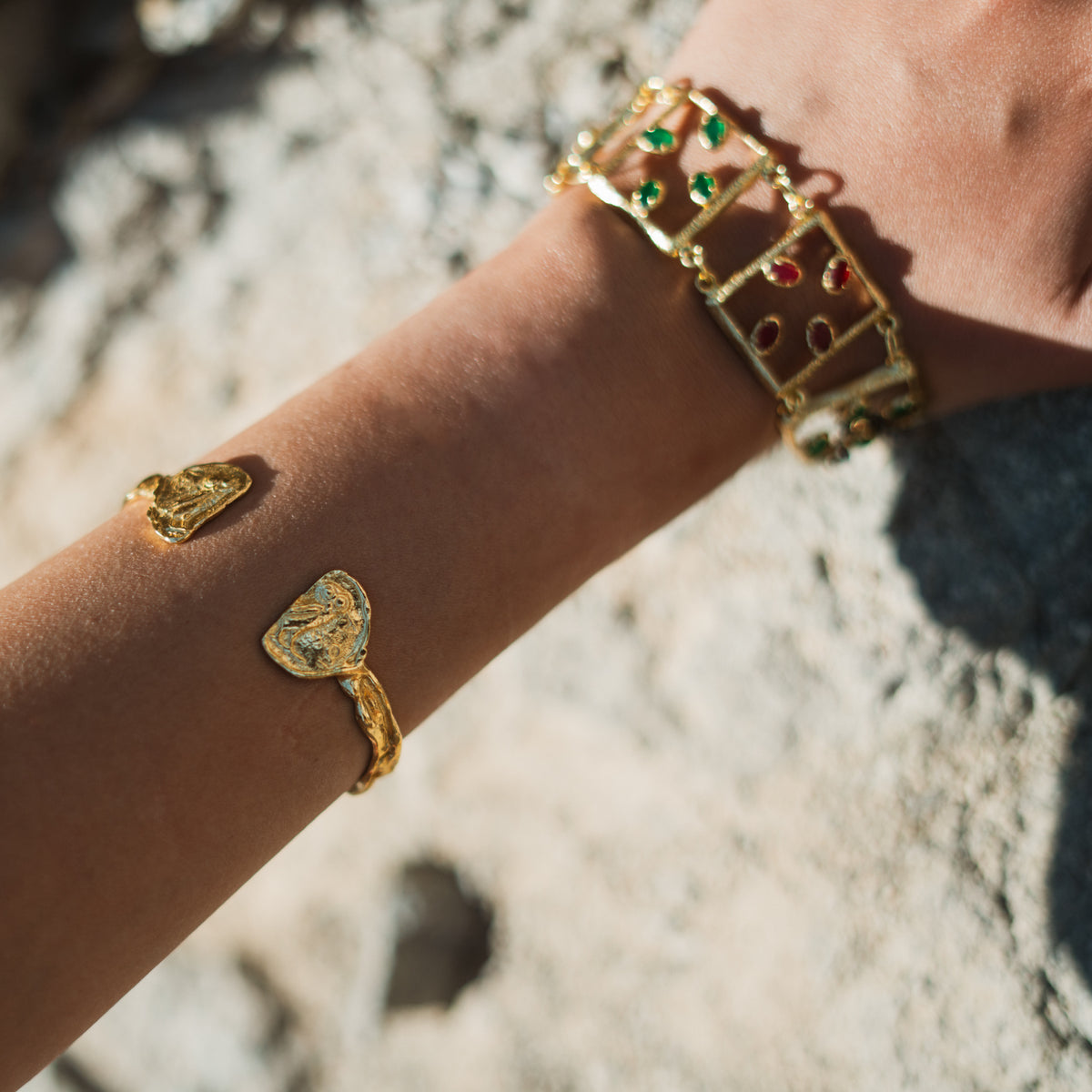 Owl coin gold cuff worn on the forearm with a gold link bracelet set with green and red stones on the wrist
