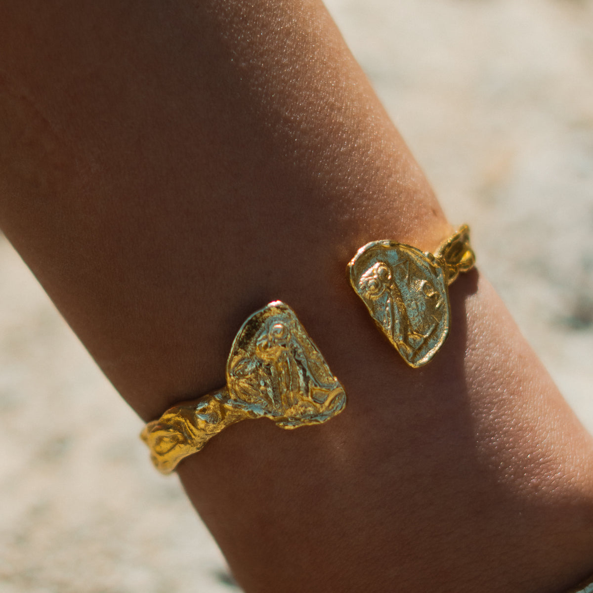 Athena owl coin ends of the hammered gold cuff bracelet on the arm in bright sunlight