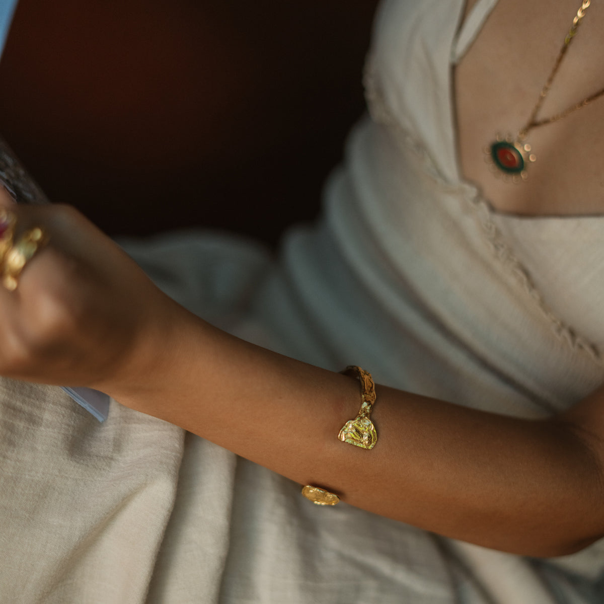 Woman in a white dress wearing the hammered gold owl coin cuff with a stone pendant necklace