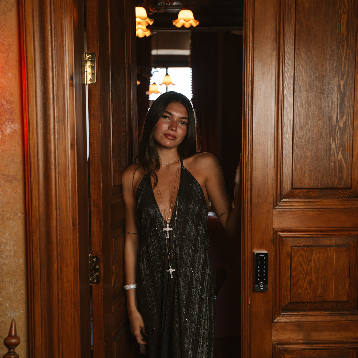Model wearing the long gold cross pendant statement necklace with a black sequined halter dress