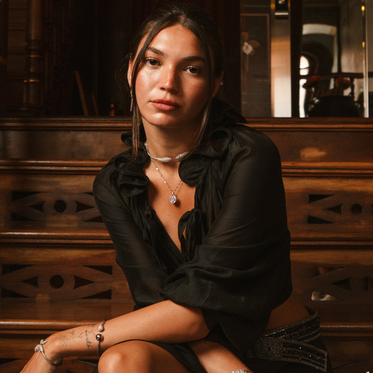 Model seated on wooden stairs wearing the silver baguette heart pendant necklace and a black blouse