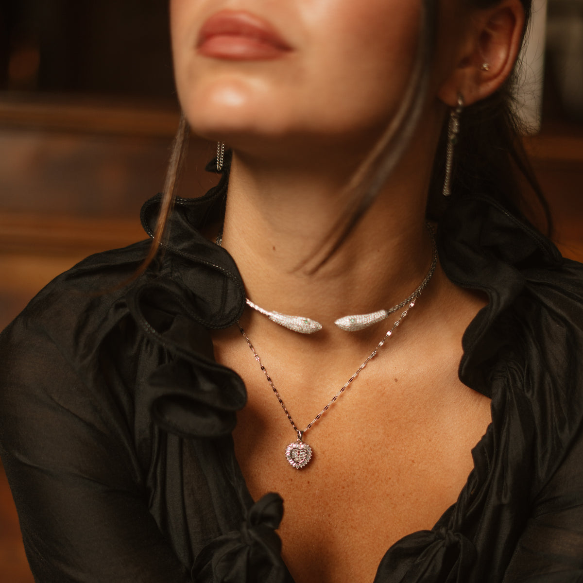 Woman in a black ruffled blouse wearing the halo heart pendant necklace layered with a silver collar
