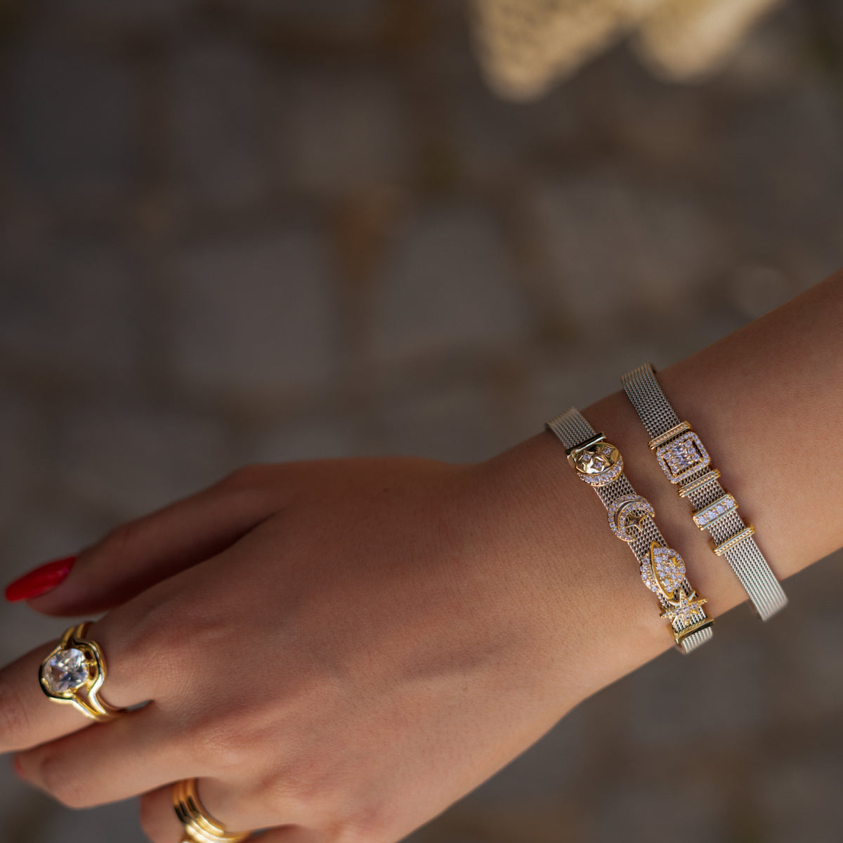 Close view of the wrist with the baguette halo charm bracelet and the moon and star charm bracelet, gold cocktail ring