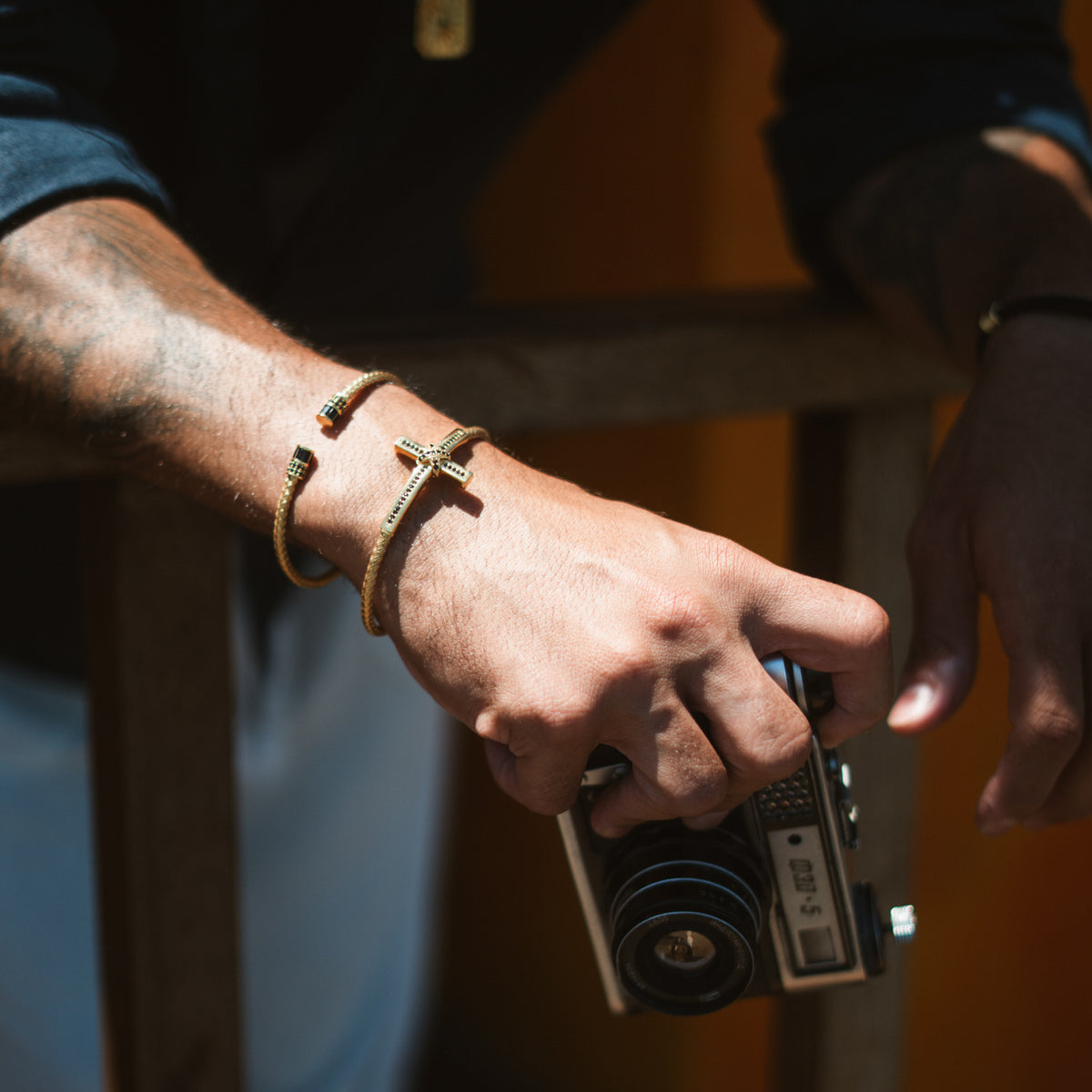 Close view of the black zircon cross cuff on a man's wrist in warm light, stacked with a thin gold cuff
