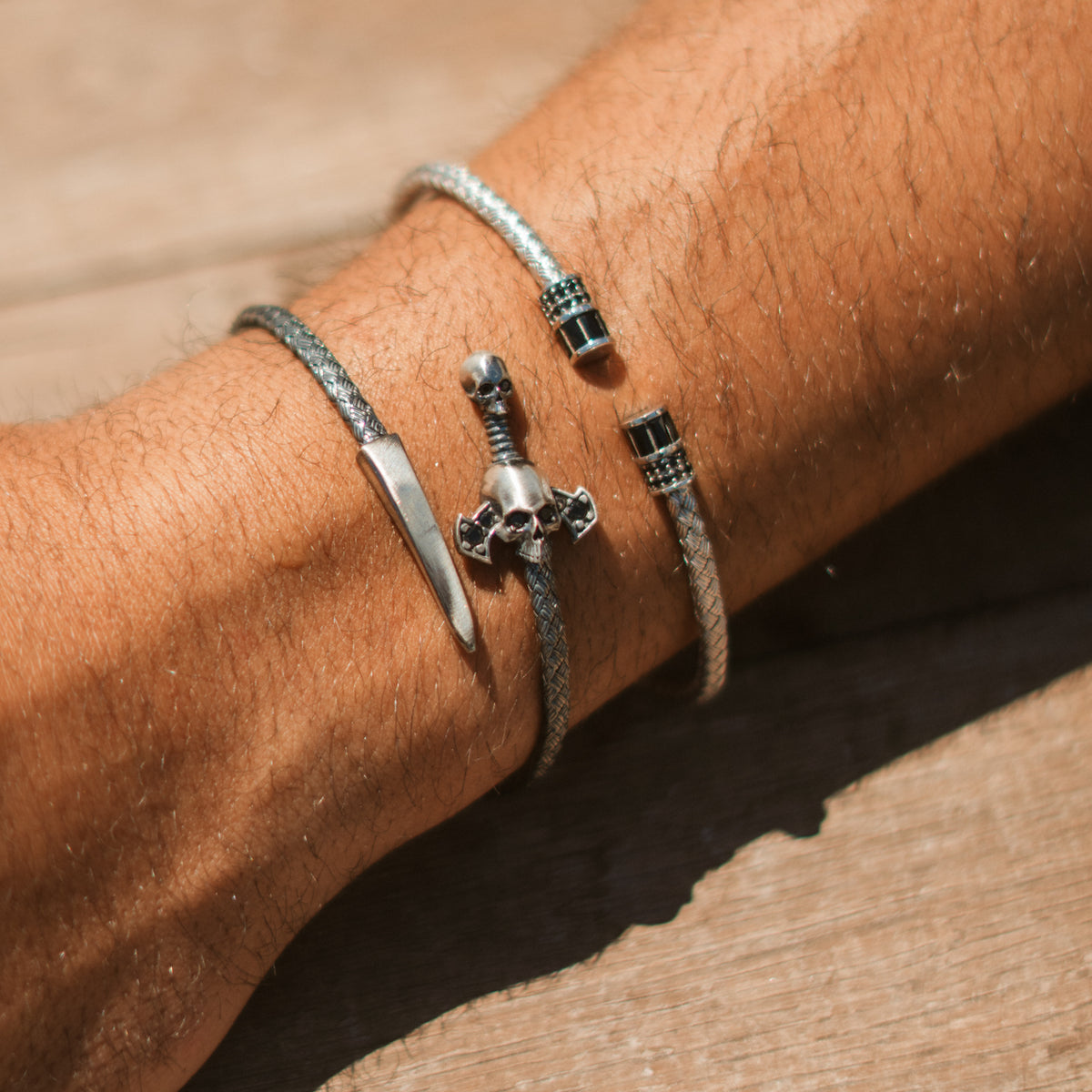 Woven sterling silver men's cuff with black barrel ends worn on the wrist, stacked with the skull and dagger wrap bracelet