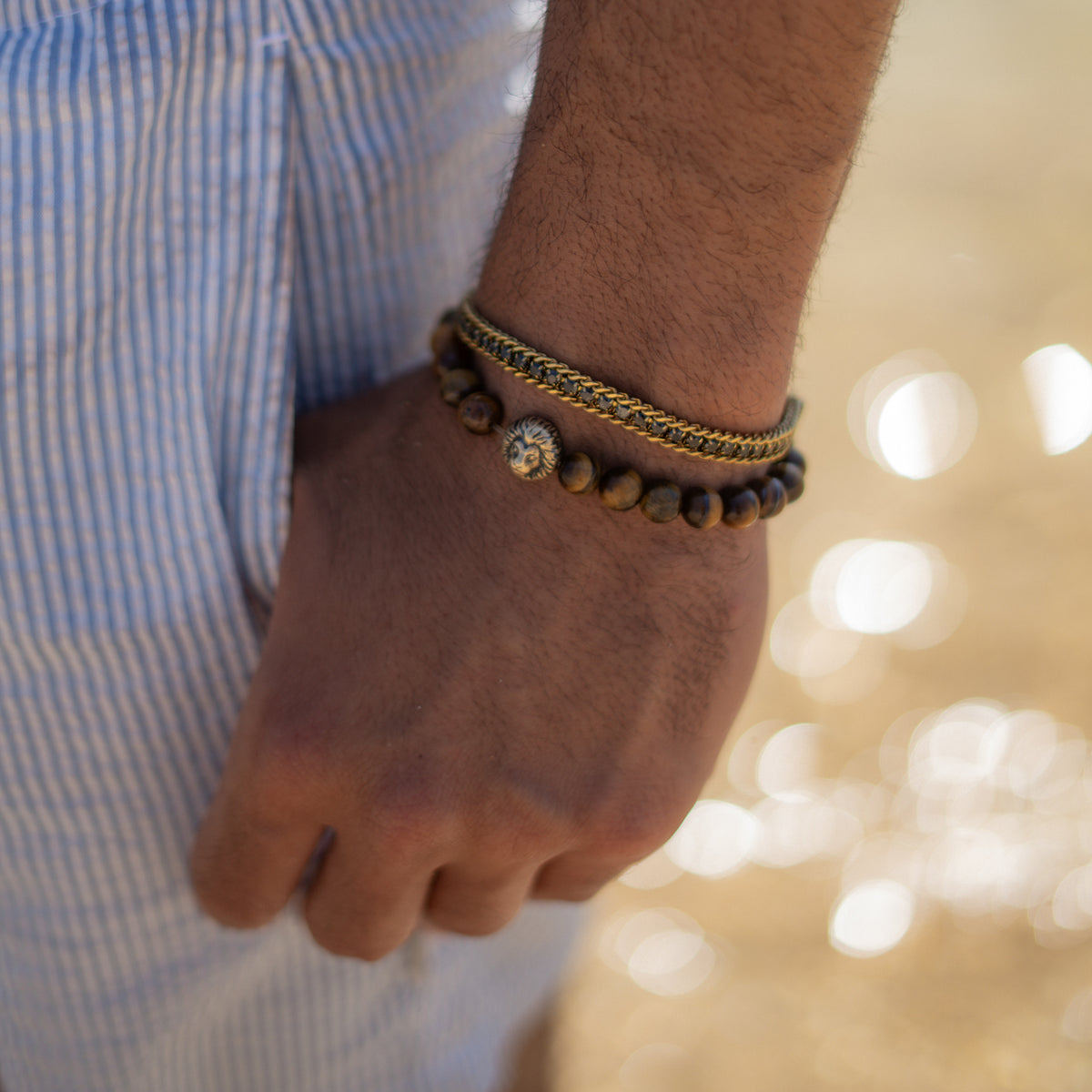Gold foxtail men's bracelet with black zircon on a wrist, hand in pocket, with a beaded bracelet in soft evening light