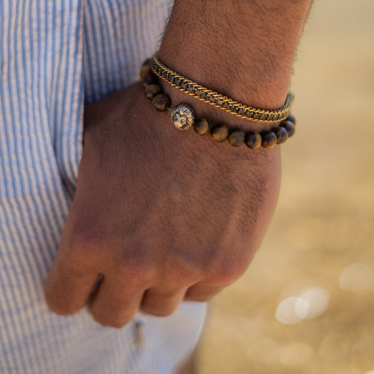 Man in a striped shirt wearing the black zircon gold foxtail bracelet stacked with a brown beaded bracelet