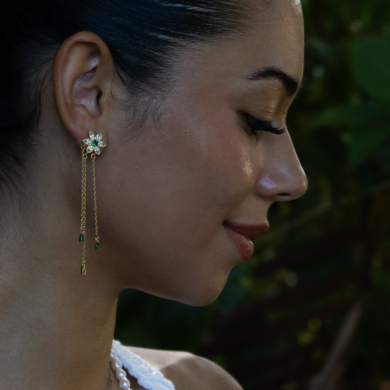 18k gold vermeil Blossom Glow drop earrings with vibrant green emerald stones, floral motif, and delicate gold chain accents.