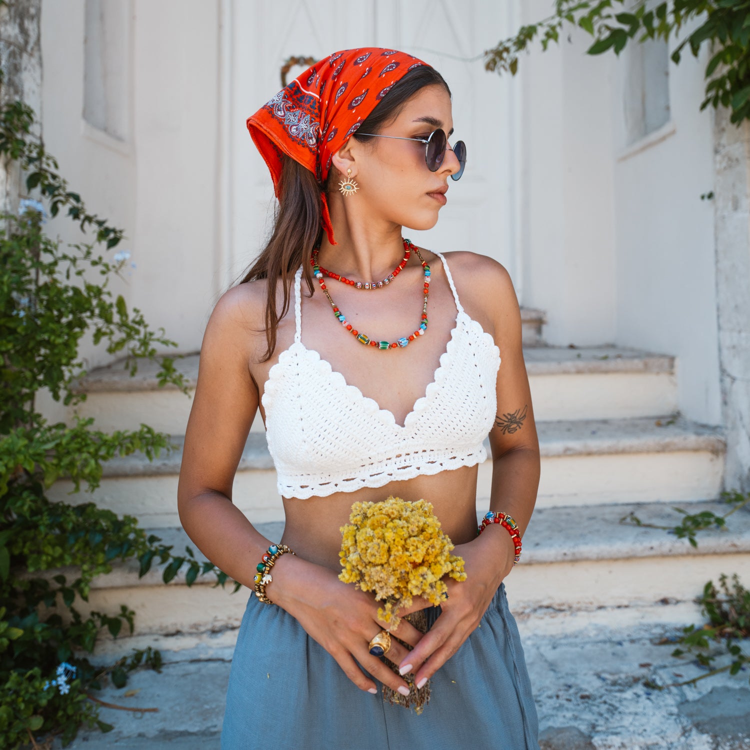 Model in red headscarf holding dried yellow flowers, wearing the colorful Carnelian Fire Energy Beaded Choker layered with a beaded necklace