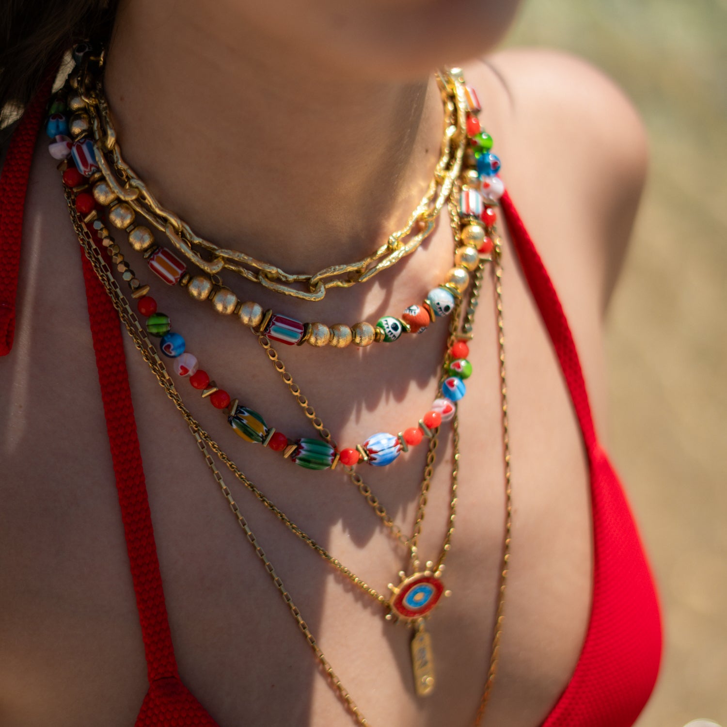 Woman wearing the Carnelian Rainbow Energy Beaded Necklace, a colorful handmade beaded necklace, layered with gold chain and skull bead necklaces