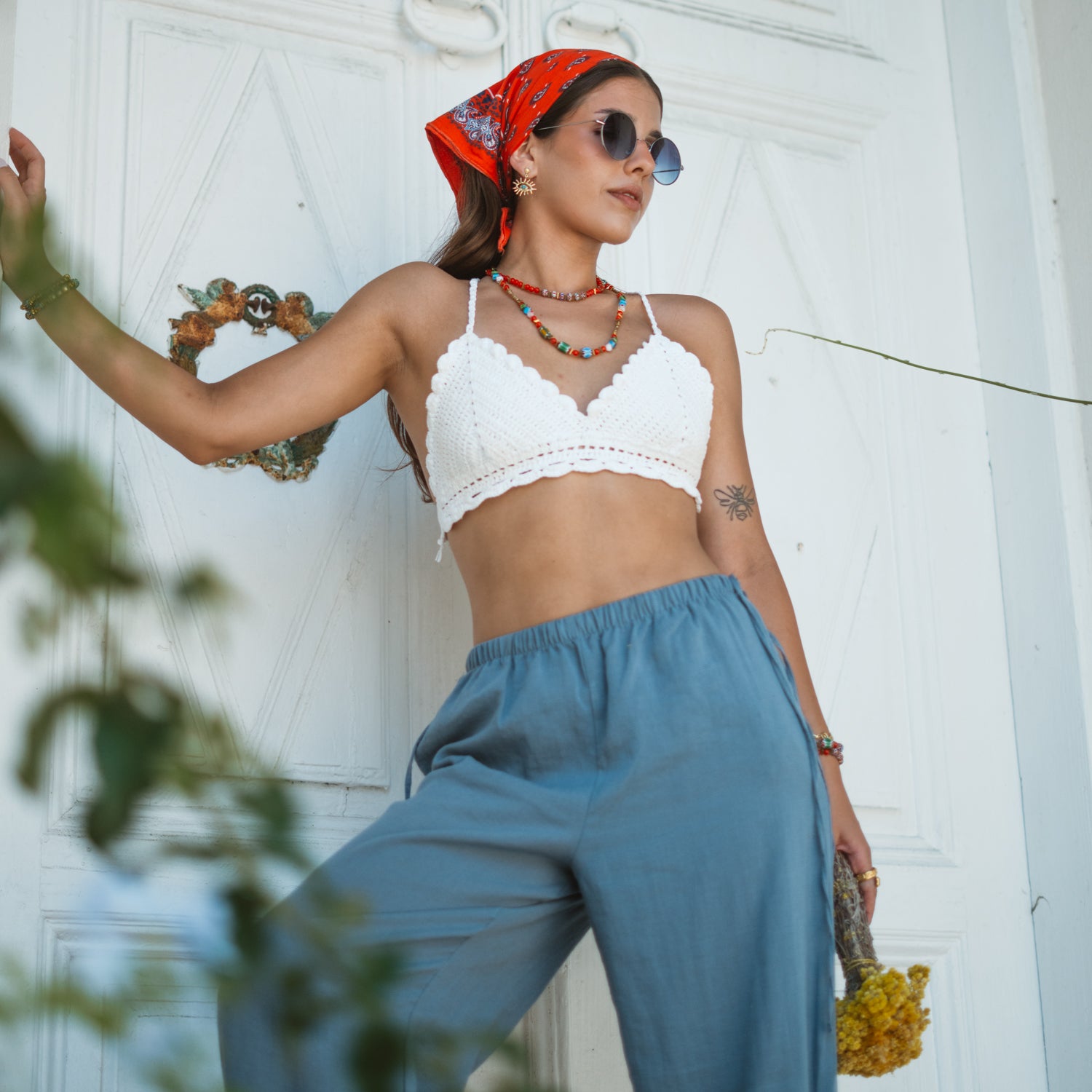 Model in a dynamic pose wearing the handmade Carnelian Rainbow Energy Beaded Necklace, a colorful energy necklace, with a white crochet top and blue linen pants