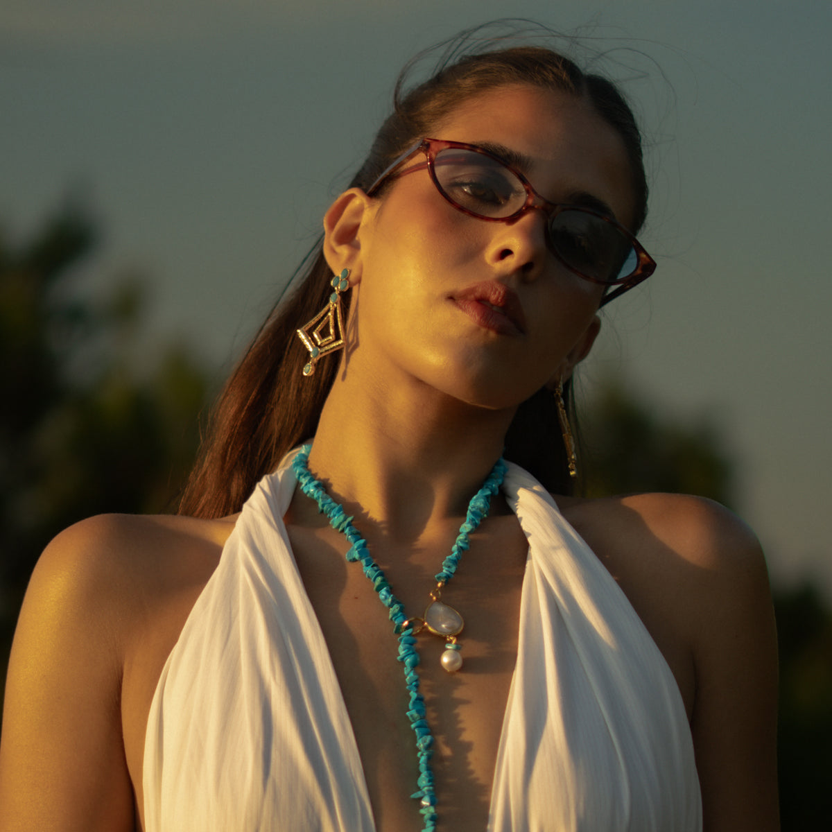 Woman with tinted glasses wearing the bohemian turquoise gold dangle earrings and a turquoise necklace