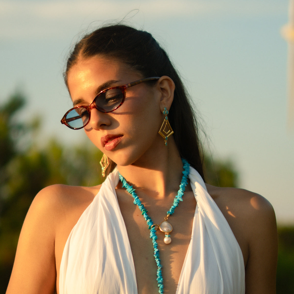 Model in a white dress against an evening sky wearing the Cleopatra turquoise kite earrings