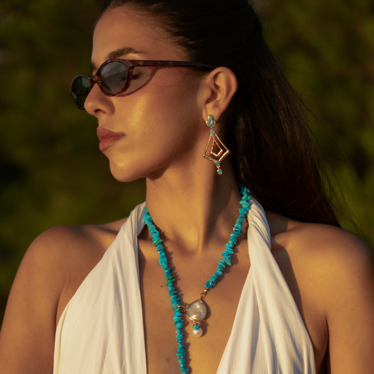 Woman in a white halter dress and sunglasses wearing the turquoise gold kite dangle earrings with a turquoise beaded necklace