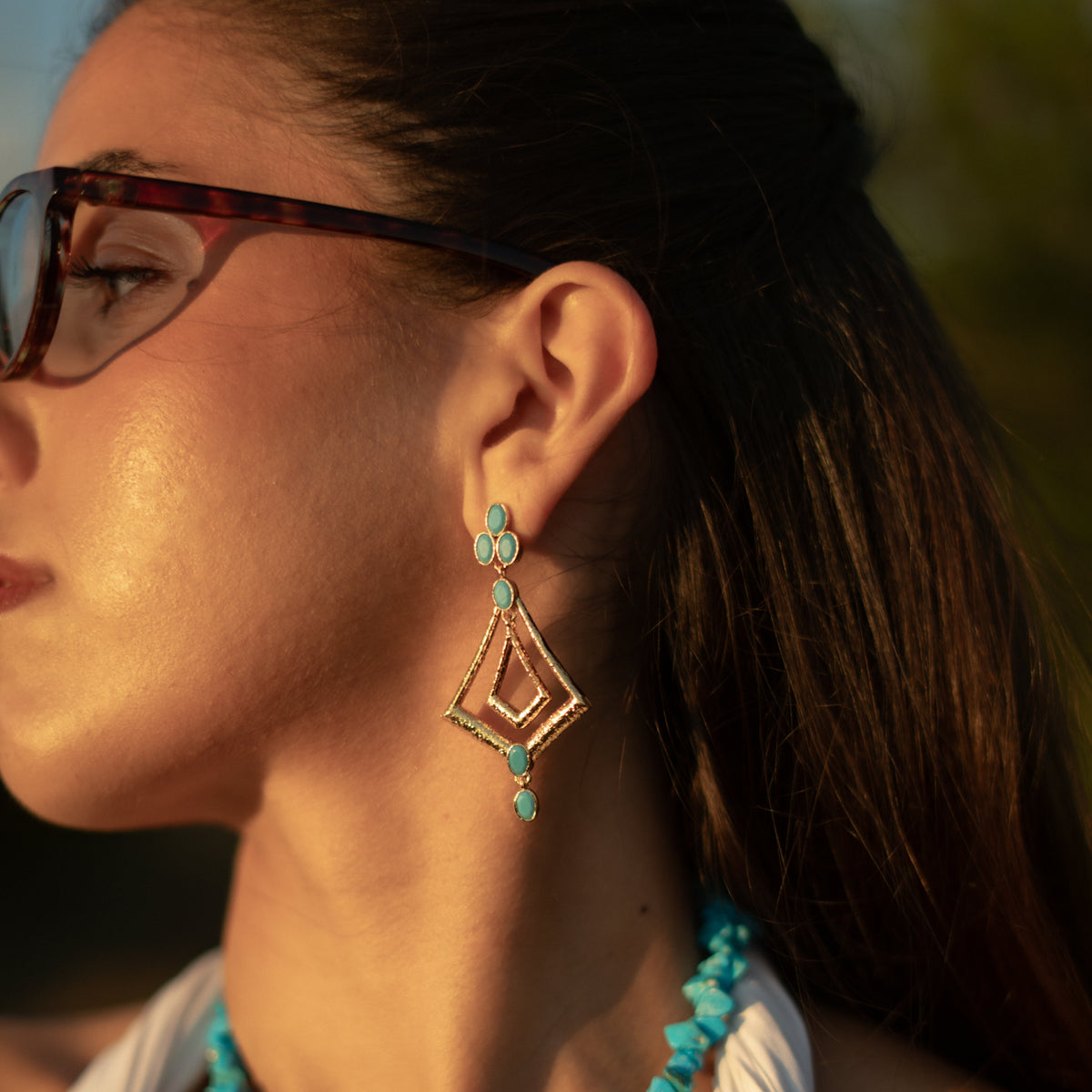 Close view of the boho turquoise gold dangle earring worn at the ear in warm golden light