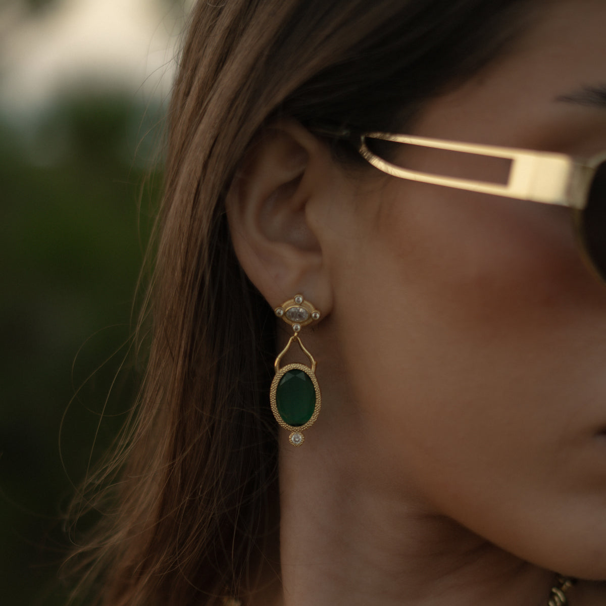 Close view of the Cleopatra Emerald drop earring on the ear, the cat eye stone reading deep green outdoors